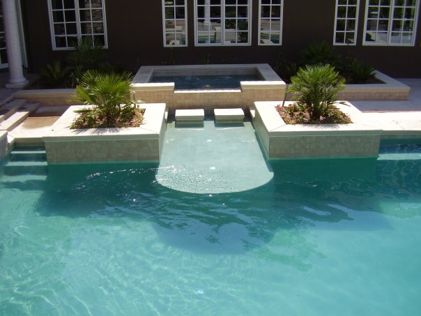 Outdoor swimming pool with stairs that has a raised underwater area accessible to the patio for sitting and laying down in