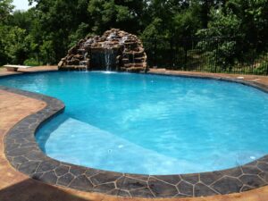 Blue backyard pool with rock waterfall feature.