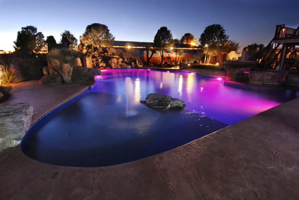 Freeform pool with color LED lighting and rock features at night
